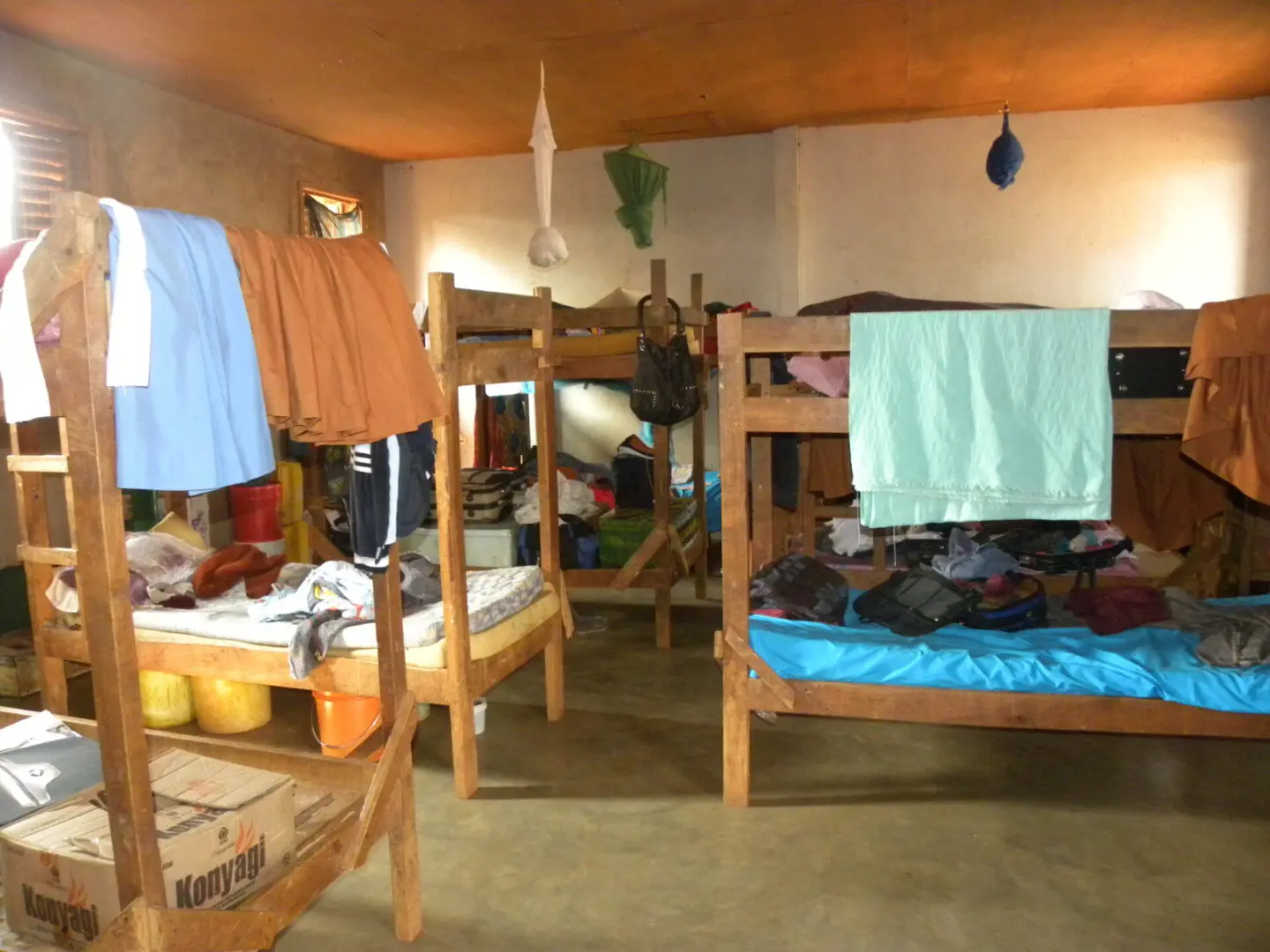 A room with several bunk beds and clothes hanging on the walls.