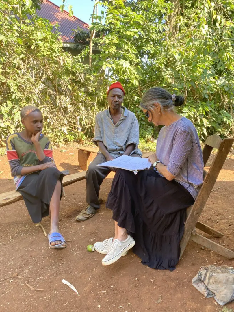 Three people sitting on a bench in the dirt.