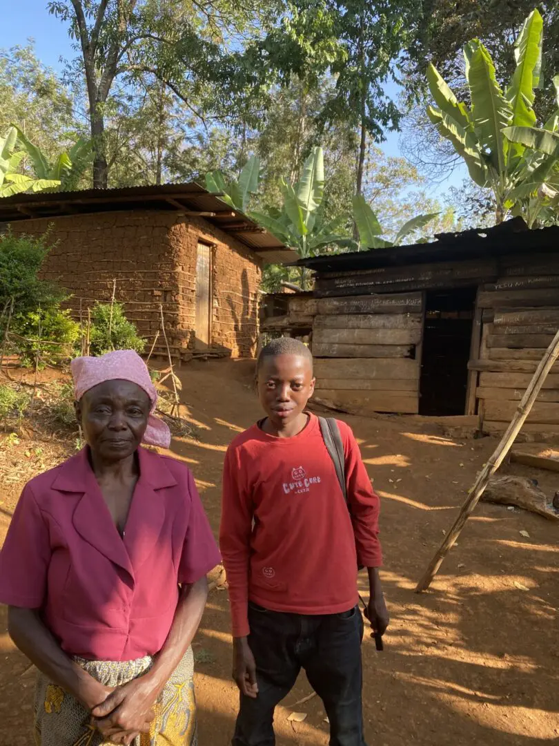 Two people standing in a dirt field near some houses.