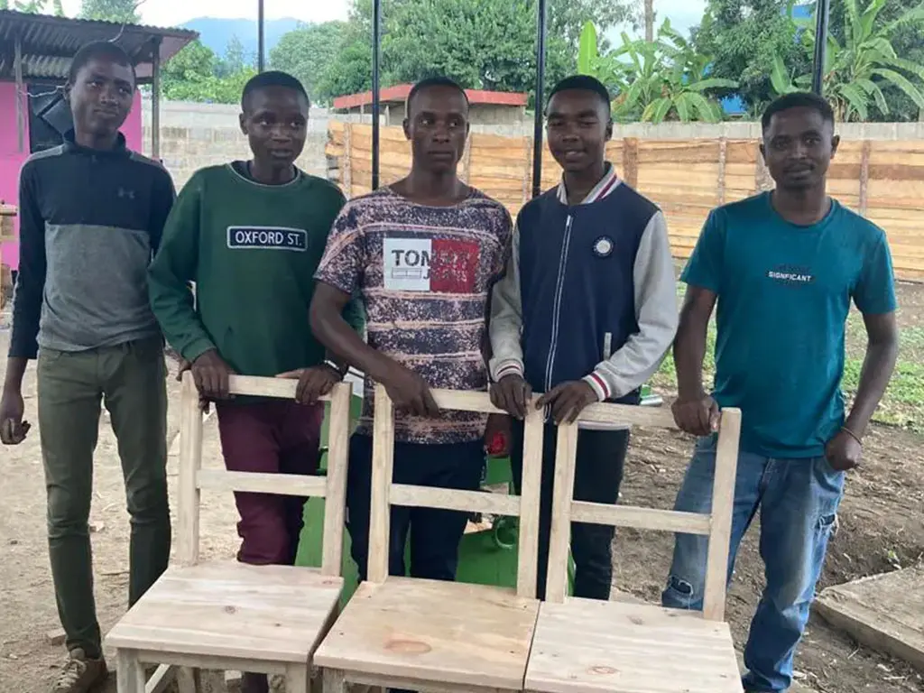 Five men stand near unfinished wooden chairs.