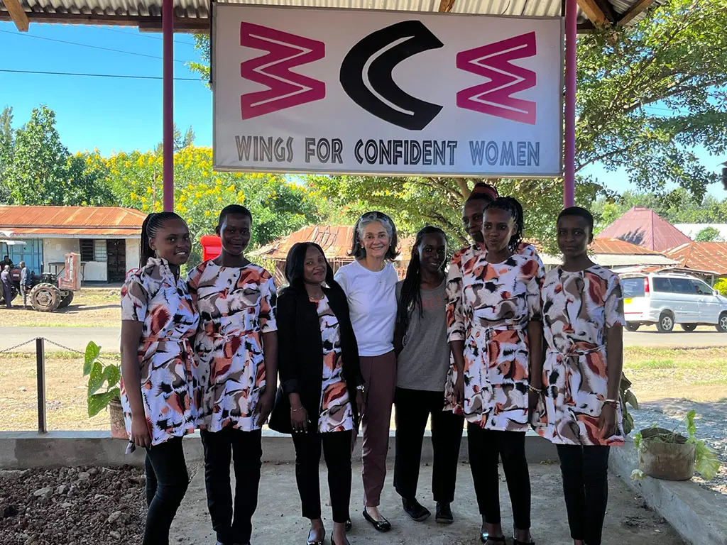 Women stand in front of a "Wings for Confident Women" sign.