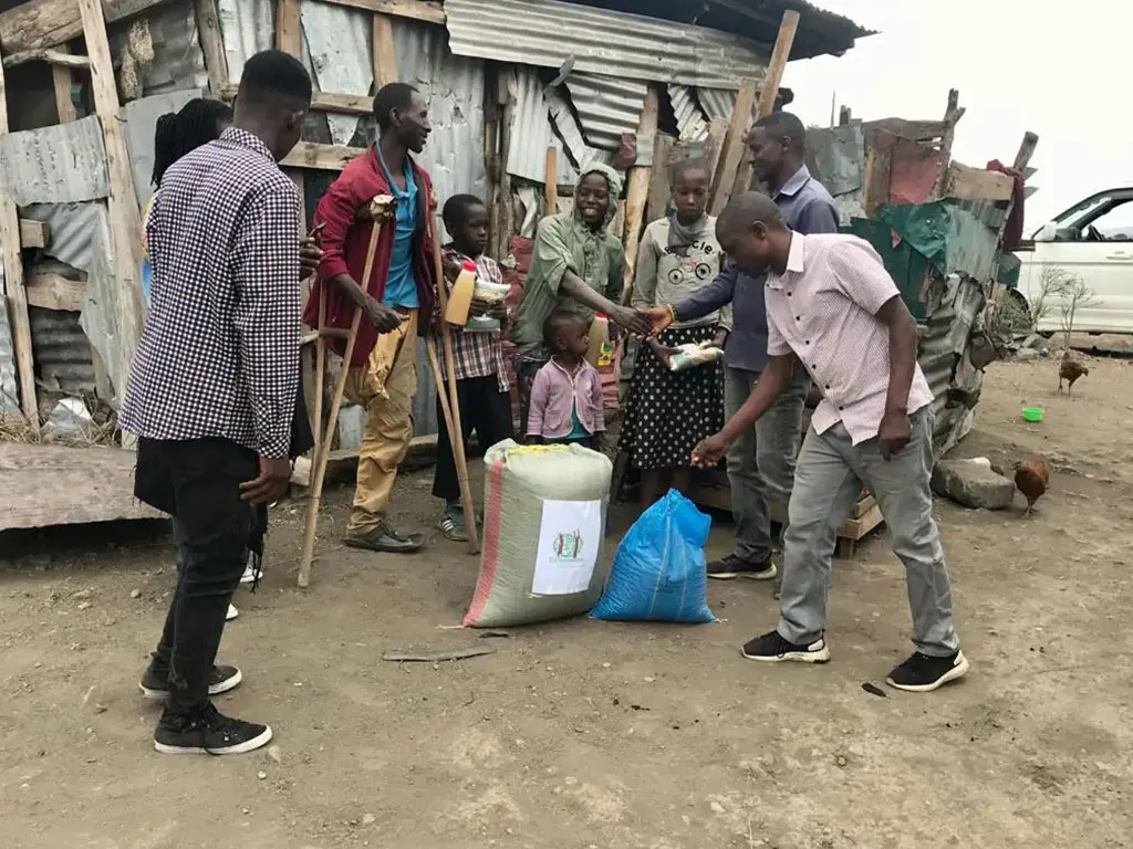 People distributing aid in front of a shack.