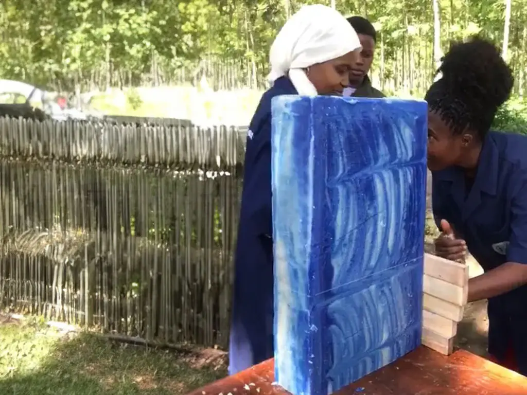 Two women cutting a large blue soap bar.