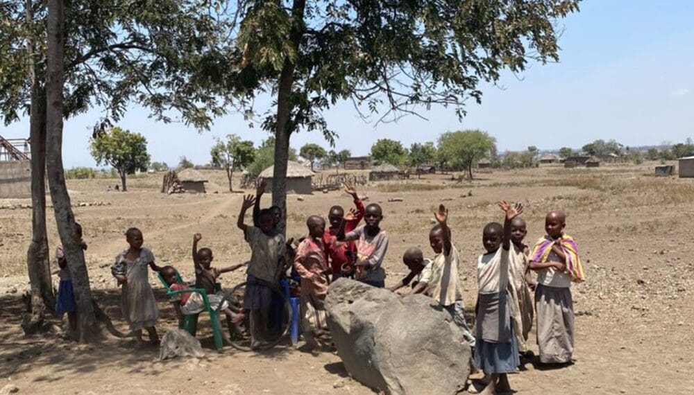 Children waving under a tree in village.