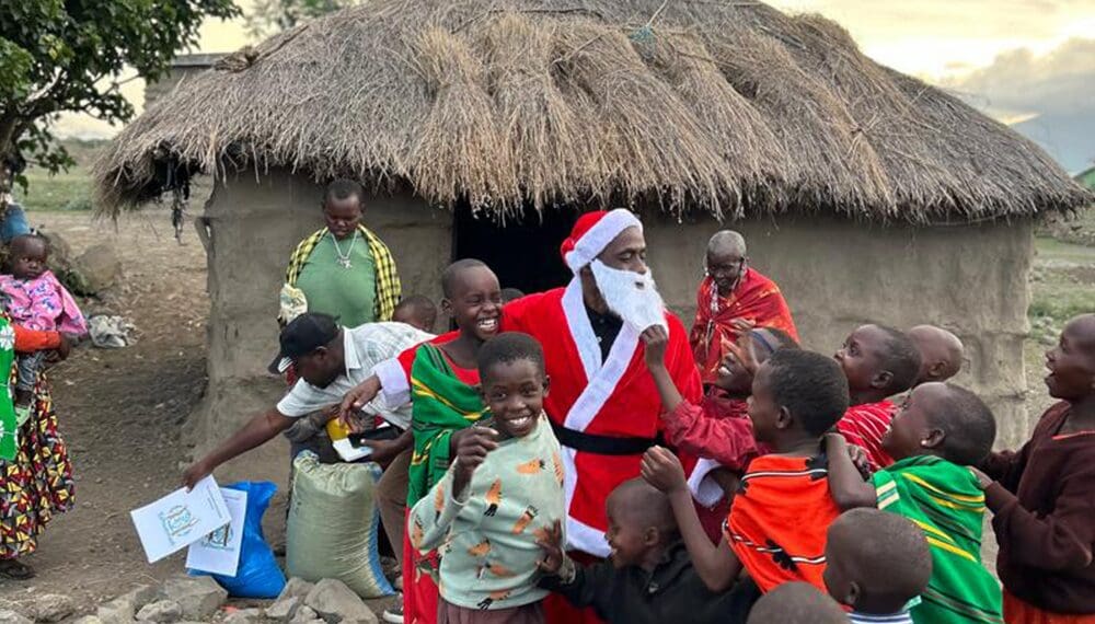 Santa with children in front of hut.